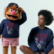A person wearing a Justice Girl sweatshirt and pink shorts is posing next to a large stuffed animal character wearing a Justice Girl sweatshirt and pink shorts.