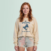 A young woman with red hair wearing a beige sweater with a graphic of a bird and the text 