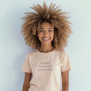 A smiling woman with curly hair wearing a light pink t-shirt with the text 