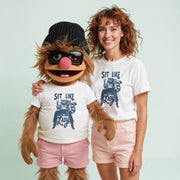 A woman and a large, furry character wearing sunglasses and a hat, both wearing white t-shirts with a graphic design.