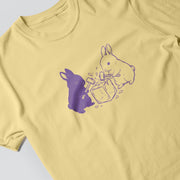 A yellow t-shirt with a graphic design featuring two rabbits, one purple and one white, interacting with a box.