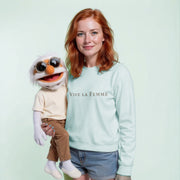 A woman with red hair is holding a white and orange stuffed animal with sunglasses on it. She is wearing a light blue sweatshirt with the text 