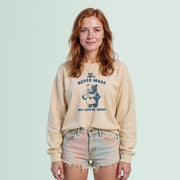 A young woman with red hair wearing a beige sweatshirt with a graphic design and text, standing against a light blue background.