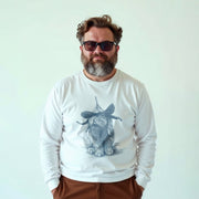 A man wearing a white long-sleeved shirt with a graphic of a rabbit wearing a hat, standing against a plain white background.