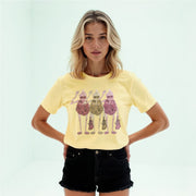 A young woman wearing a yellow t-shirt with a graphic design of three stylized figures, standing in front of a plain white background.