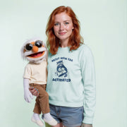 A woman with red hair is holding a large, white stuffed animal with sunglasses on its head. The stuffed animal is wearing a shirt with the text 