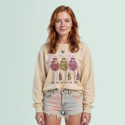 A young woman with red hair wearing a beige sweater with a graphic design of three cartoon-like figures, and denim shorts.