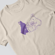 a t-shirt with a graphic design depicting two rabbits, one purple and one white, interacting with a box.