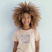 A smiling woman with curly hair wearing a light pink t-shirt with a graphic design.