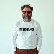 A man with a beard wearing a white long-sleeved shirt with the word 