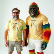 Two men wearing yellow t-shirts with a graphic design stand next to a gorilla wearing a yellow t-shirt with a similar graphic design.