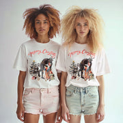 Two young women wearing white t-shirts with Christmas-themed graphics stand side by side against a white background.