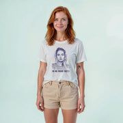 A woman with red hair wearing a white t-shirt with a graphic design and text, standing against a light blue background.