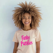 A smiling woman with curly hair wearing a pink t-shirt with the text 