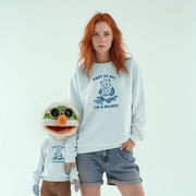 A woman with red hair wearing a white sweatshirt with a graphic and text, and a smaller stuffed animal wearing a similar sweatshirt, standing together against a white background.