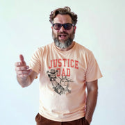 A man with a beard wearing a t-shirt with a graphic design and text, smiling and gesturing with his hand.