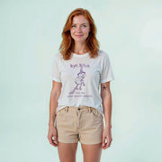 A woman with red hair wearing a white t-shirt with a graphic design and text, standing against a light blue background.