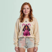 A young woman with red hair wearing a beige sweater with a graphic design and denim shorts stands against a light blue background.