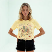 A young woman with blonde hair wearing a yellow t-shirt with a floral design and black shorts stands with her hands on her hips.