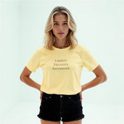 A young woman with blonde hair wearing a yellow t-shirt with the text 