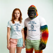 A woman wearing a white t-shirt with a graphic and text, and a man wearing a white t-shirt with a graphic and text, standing next to a gorilla with colorful fur.