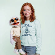 A woman with red hair is holding a large stuffed animal, which appears to be a character from a children's television show or movie. The woman is wearing a light blue sweatshirt with a humorous text printed on it.