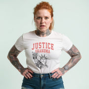 A woman with red hair wearing a white t-shirt with a graphic design and text, standing with her hands on her hips.