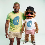 A man in a yellow t-shirt and khaki shorts stands next to a large, furry mascot wearing a white t-shirt, pink shorts, and a black hat.