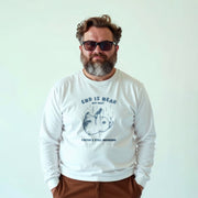 A man wearing a white long-sleeved shirt with a graphic design and text printed on it, standing against a plain white background.