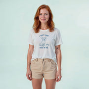A woman with red hair wearing a white t-shirt with a graphic design and text, standing against a light blue background.