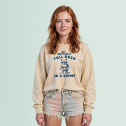 A young woman with red hair wearing a beige sweatshirt with a graphic design and text, standing against a light blue background.