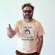 A man with a beard wearing a t-shirt with a graphic and text, smiling and gesturing with his hand.