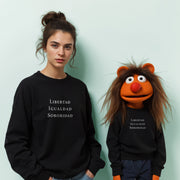 A woman wearing a black sweater with white text stands next to a large orange character wearing a black sweater with white text.