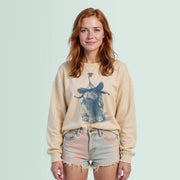 A young woman with red hair wearing a beige sweater with a blue illustration of a cat and denim shorts, smiling at the camera.