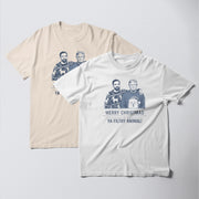 two t-shirts with a humorous Christmas-themed design. The t-shirt on the left has a beige background with a graphic of two men wearing Christmas sweaters, and the text 