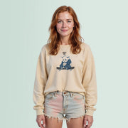 A young woman with red hair is standing against a light blue background, wearing a beige sweater with a graphic of a panda on it and denim shorts.