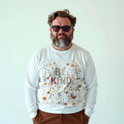 A man with a beard wearing a white long-sleeved shirt with a floral design and the text 