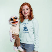 A woman with red hair is holding a large stuffed animal, which appears to be a puppet or a character, and she is wearing a light blue sweatshirt with a graphic design on it.