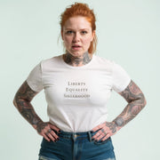 A woman with red hair and tattoos is wearing a white t-shirt with the text 