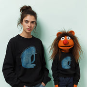 A woman wearing a black sweatshirt with a blue elephant graphic stands next to a large orange character wearing a black sweatshirt with a blue elephant graphic.