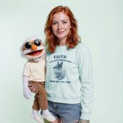 A woman with red hair is holding a large, white, cartoonish cat puppet with sunglasses on its face. The woman is wearing a light blue sweatshirt with a graphic design and text printed on it.