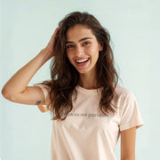 A smiling woman with long brown hair wearing a white t-shirt with text on it.