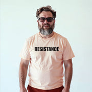 A man with a beard wearing a peach-colored t-shirt with the word 