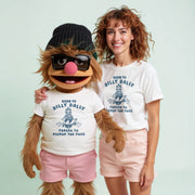 A woman wearing a white t-shirt with a graphic of a character from the Muppets and a matching hat stands next to a large stuffed animal character wearing a white t-shirt with a similar graphic and text.