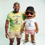 A man in a yellow t-shirt and khaki shorts stands next to a large, furry mascot wearing a white t-shirt and pink shorts, both smiling and posing for the camera.