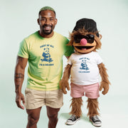 A man in a green t-shirt and khaki shorts stands next to a large, furry mascot wearing a white t-shirt and pink shorts, both smiling and posing together.