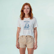A woman with red hair wearing a white t-shirt with a graphic and text, standing against a light blue background.