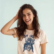 A smiling woman with long brown hair wearing a white t-shirt with a graphic design.
