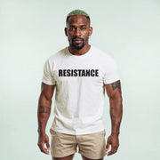 A man with green hair and a serious expression wearing a white t-shirt with the word 