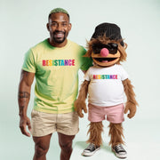 A man in a yellow t-shirt and khaki shorts stands next to a large, furry mascot wearing a white t-shirt and pink shorts, both with the word 